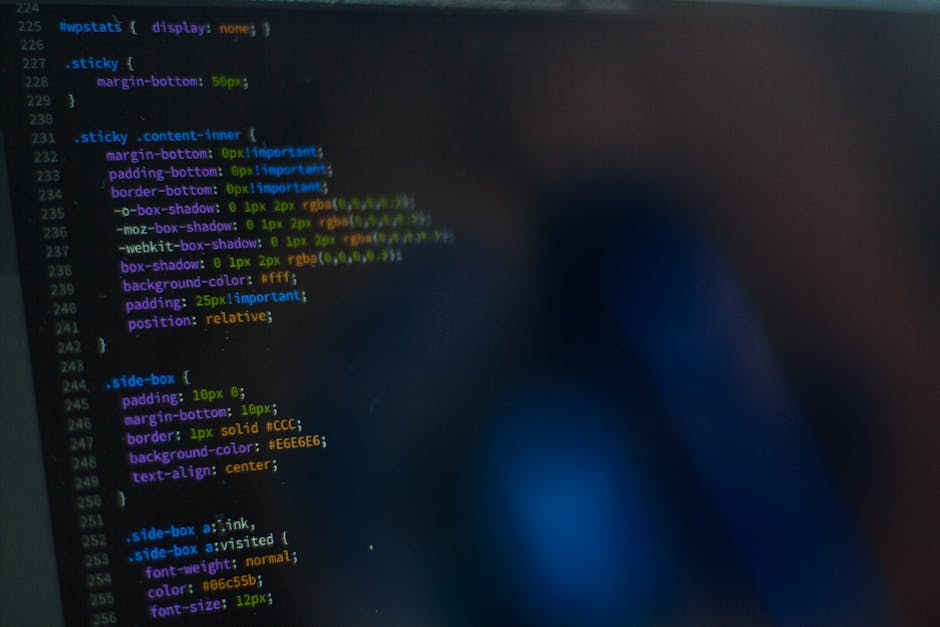 Close-up view of a computer screen displaying colorful lines of programming code with syntax highlighting in green, yellow, orange, and pink on a dark background, indicative of a software development 